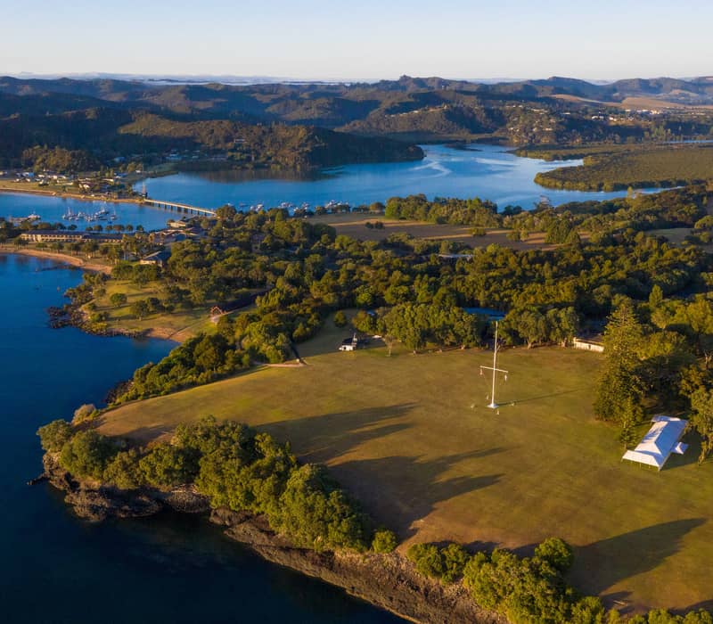 Aerial view of coastal landscape with islands, harbor, trees, and clear blue water at Waitangi Treaty Grounds. Credit: Waitangi Treaty Grounds