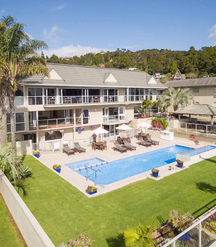 Outdoor swimming pool at Kingsgate Hotel Autolodge with lounge chairs, palm trees, and green lawn on a sunny day. Credit: Kingsgate Hotel Autolodge Paihia