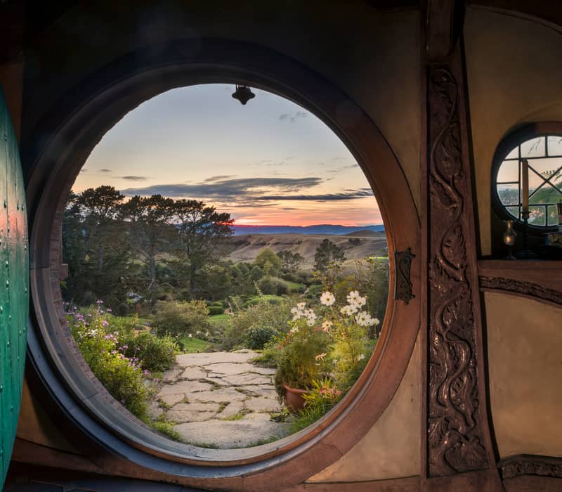 View through a round hobbit door opening to a garden and hills at sunset Credit: Entrada - Gray Line / Great Sights