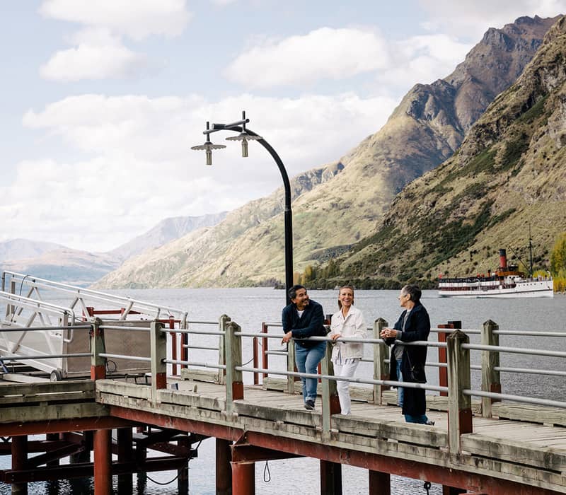Visitors on a pier overlooking a lake with a steamship at Walter Peak High Country, Queenstown.