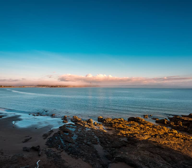 A wide beach at sunrise with golden rocks and mist. Credit: Fine Tours Group