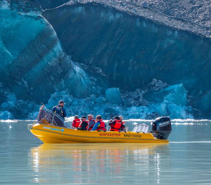 Group of tourists in yellow boat touring near a blue glacier with rocky mountain background. Credit: The Hermitage Hotel