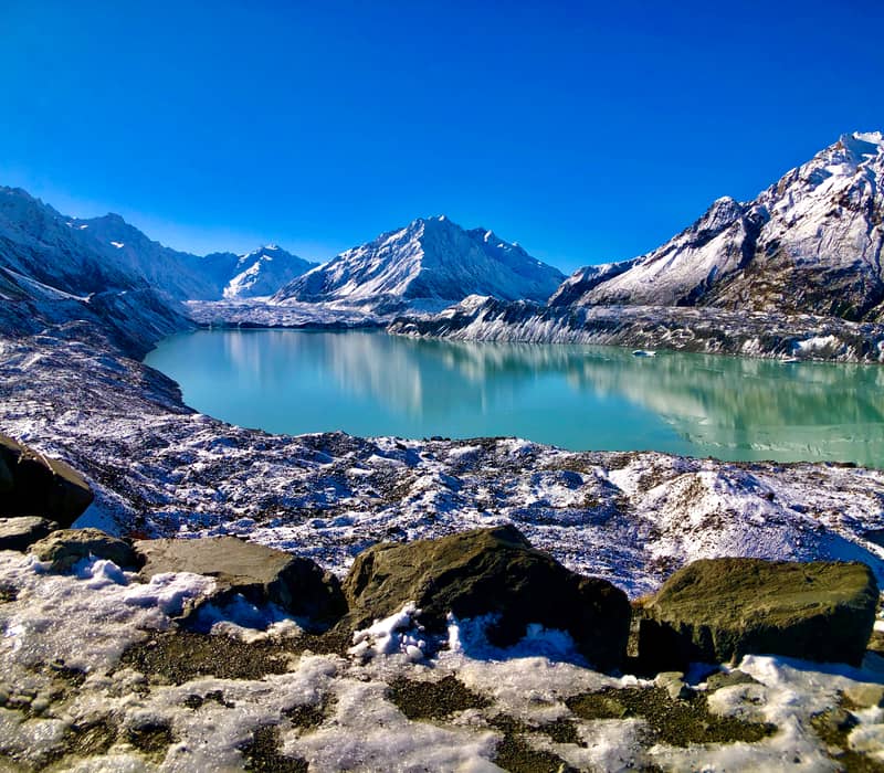 Glacial lake with snowy mountains and rocks under clear blue sky Credit: Cheeky Kiwi - Aoraki Mt Cook