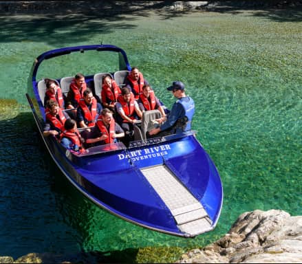 Group of people wearing life jackets on a blue jetboat in clear green river water with a guide. Credit: Dart River Safaris