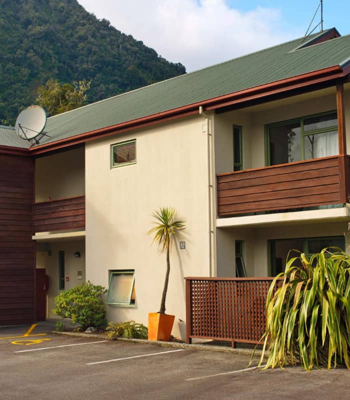 Two-story motel building with balconies and parking in front, with a green mountain behind. Credit: Punga Grove Motel & Suites