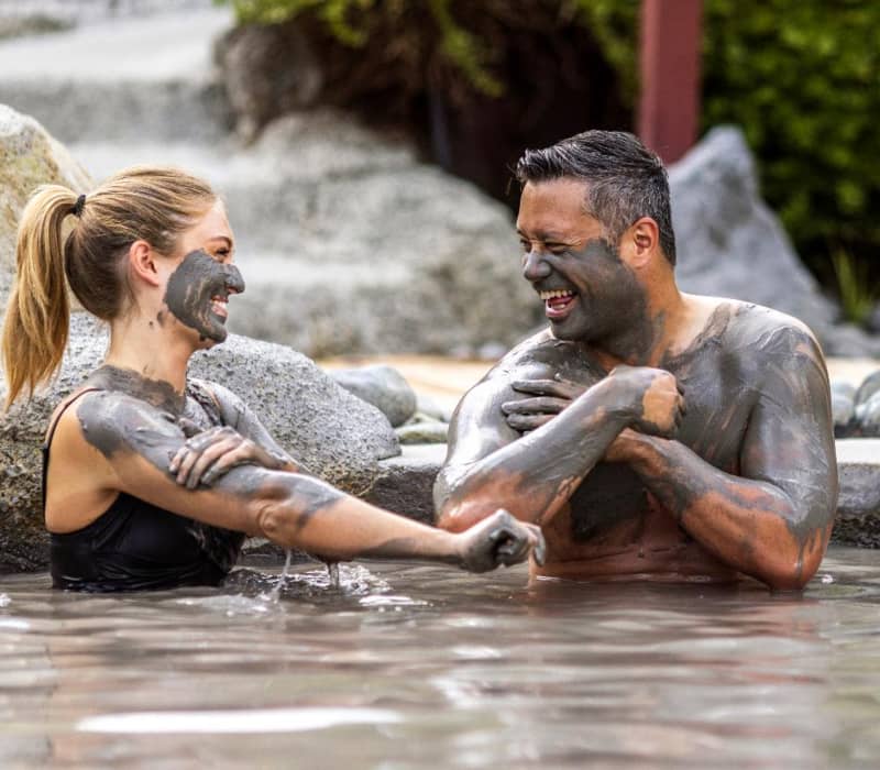 Happy couple covered in mud enjoying a mud bath outdoors, smiling and having fun. Credit: Hell's Gate