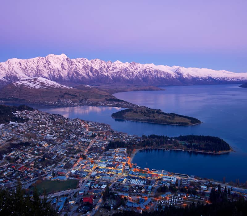 Aerial image of Queenstown at dusk with snow-covered mountains and lake in winter. Credit: New Zealand Fine Touring