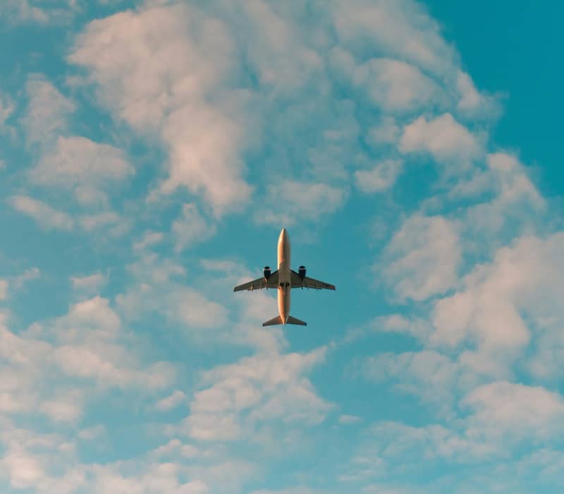 An airplane seen from directly below flying high in a bright blue sky scattered with fluffy white clouds. Credit: Photo by Philip Myrtorp on Unsplash
