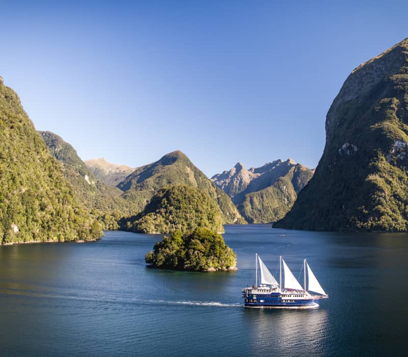 Sailboat navigating a picturesque fjord with green mountains and clear blue sky.