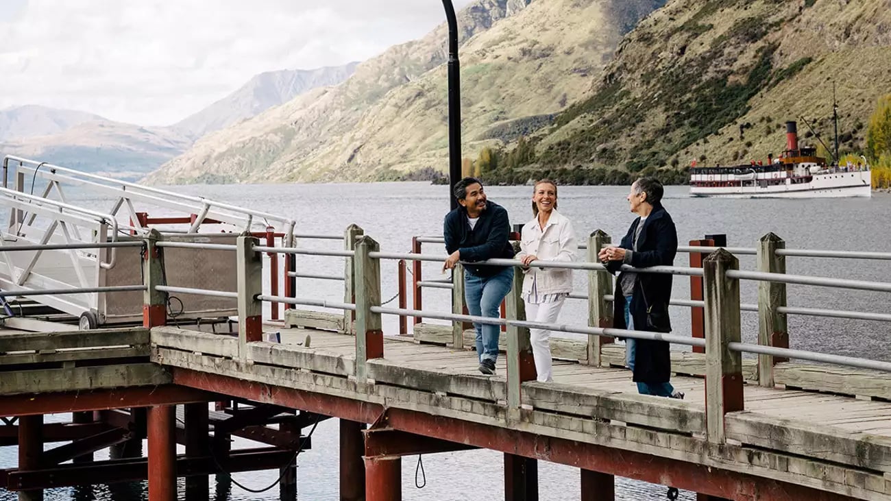 Visitors on a pier overlooking a lake with a steamship at Walter Peak High Country, Queenstown.
