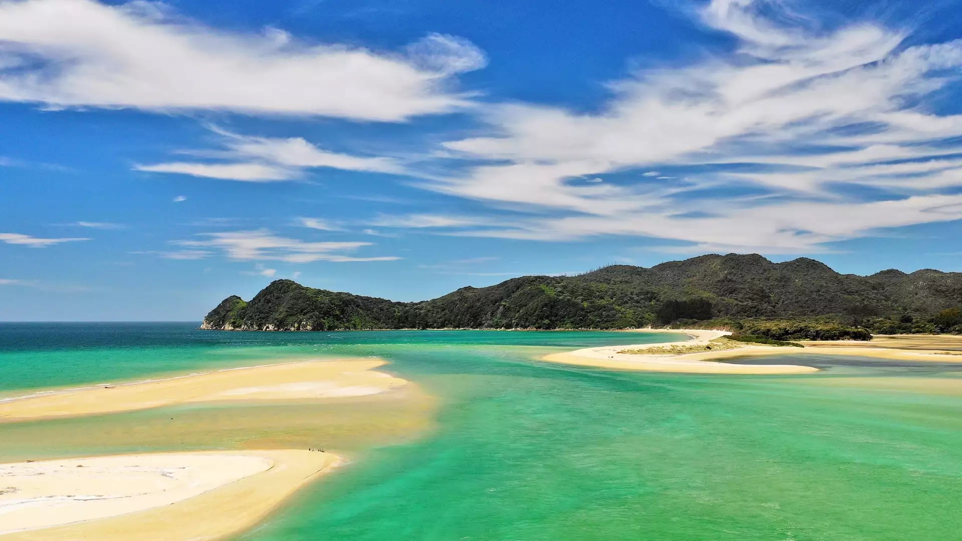 Sandy beach with turquoise water, green hills, and blue sky with clouds. Credit: Pure Discoveries