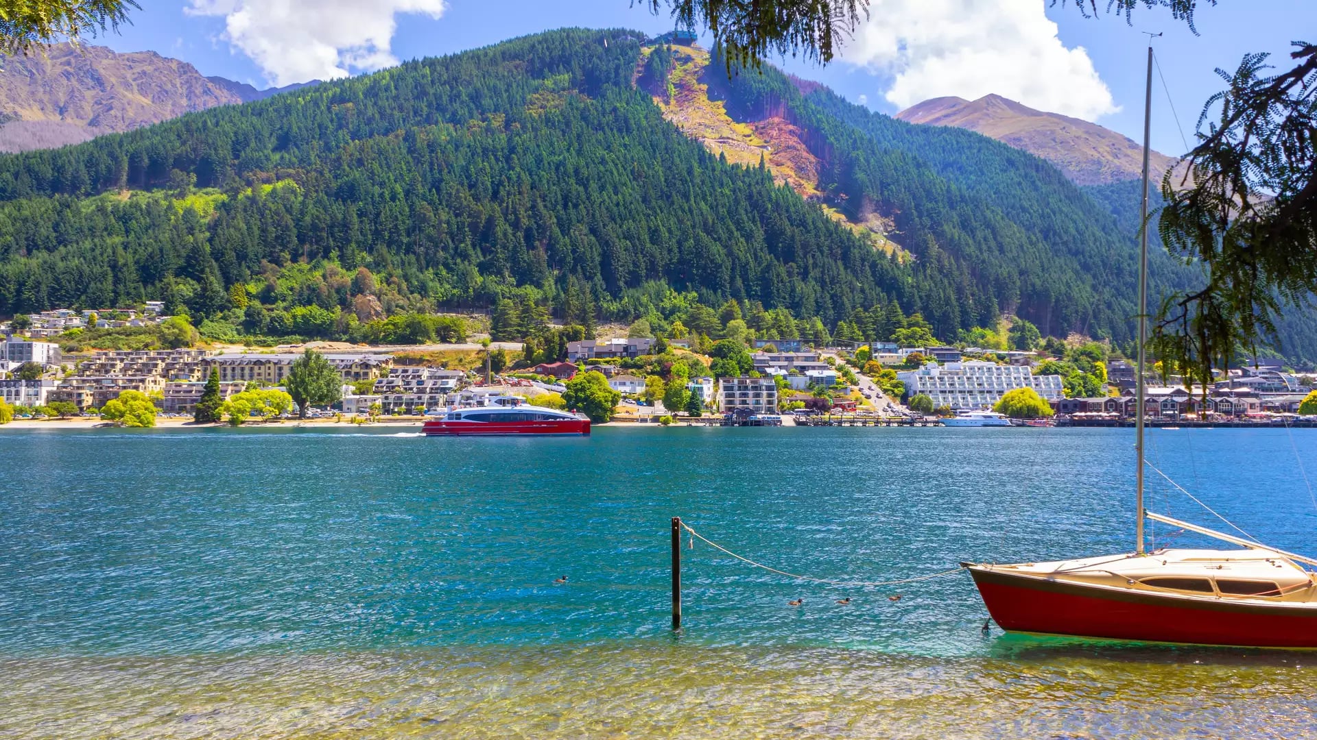 Looking out over Lake Wakatipu in Queenstown with a green hill and boats on the lake Credit: New Zealand Fine Touring - Photographer Unknown