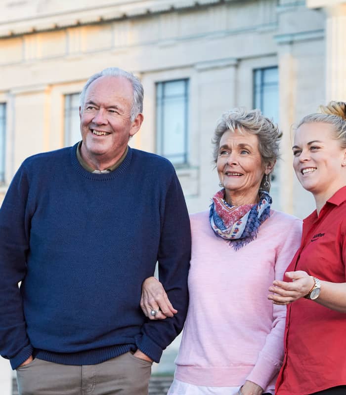 Senior couple with a tour guide standing outside a historic building in Auckland. Credit: AAT Kings