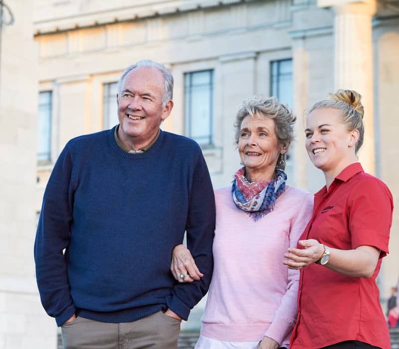 Senior couple with a tour guide standing outside a historic building in Auckland. Credit: AAT Kings