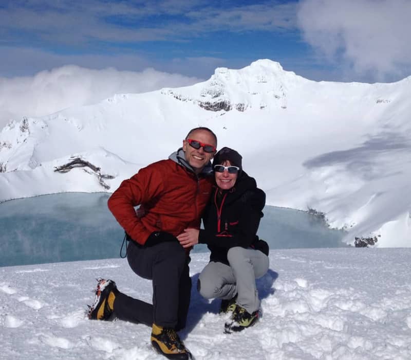 Hikers posing at the snowy summit of a volcano overlooking a turquoise crater lake. Credit: Adrift Tongariro