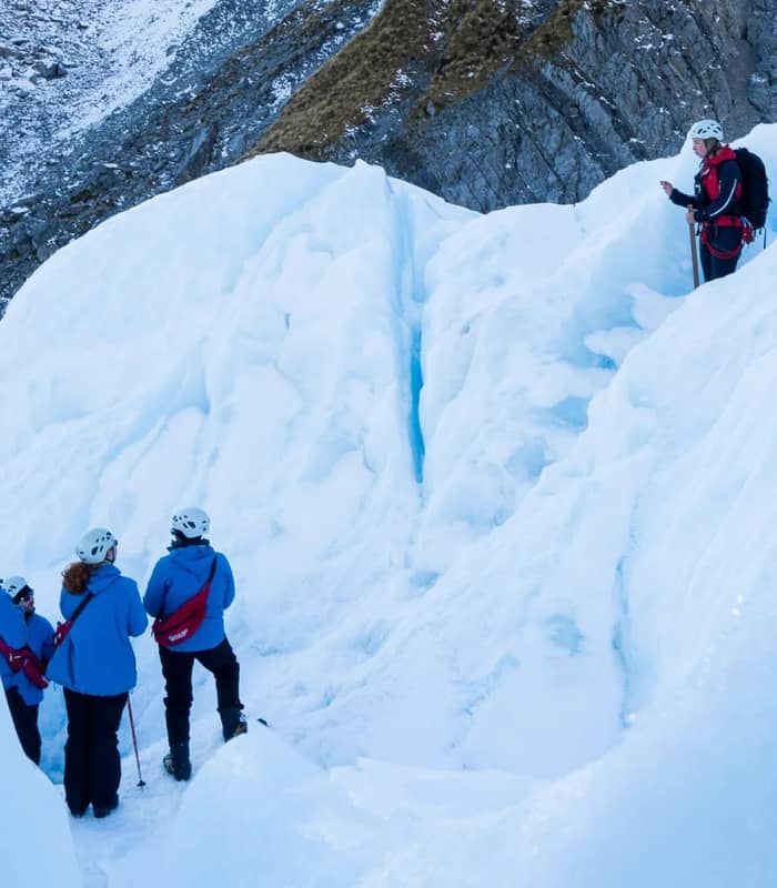 Group of people ice trekking with guide on Franz Josef Glacier snowy and icy terrain. Credit: Franz Josef Glacier Guides