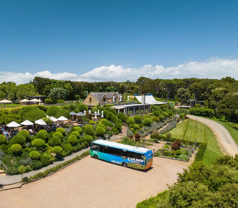 Tour bus parked near a garden with outdoor seating and green bushes under sunny, clear blue skies. Credit: Fullers 360