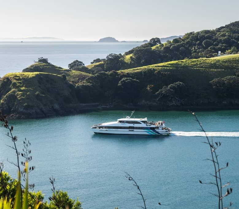 Ferry cruising in blue ocean beside green hills and trees on an island. Credit: Fullers 360