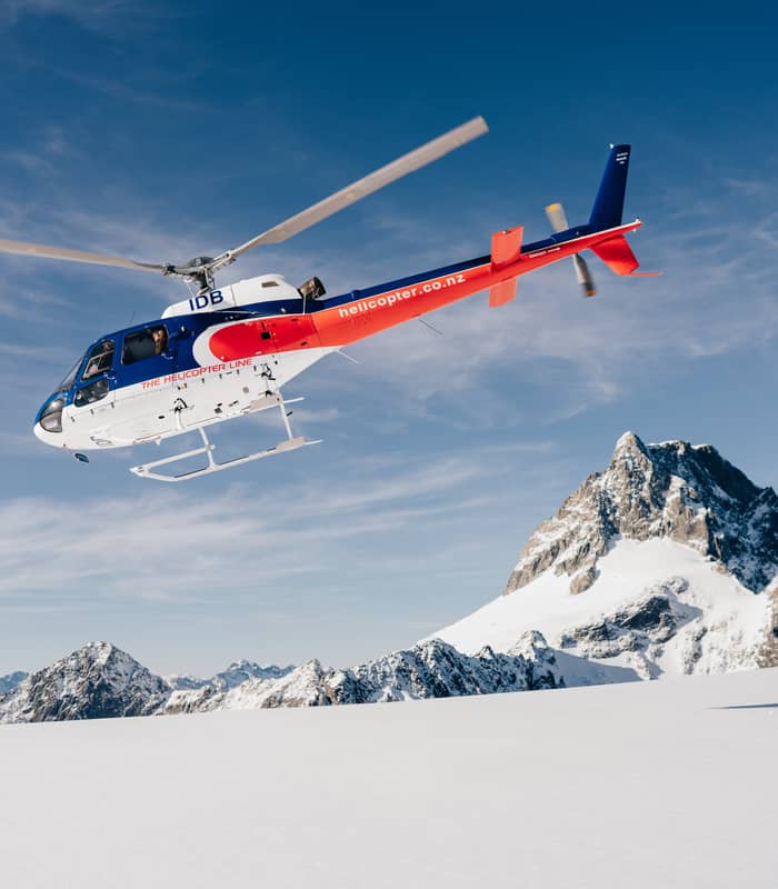 Helicopter flying over snowy mountain peak under blue sky. Credit: The Helicopter Line