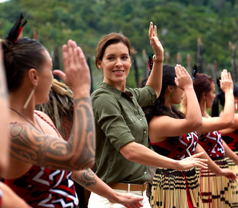 Group of women in traditional Maori attire performing a dance with raised hands outdoors. Credit: Pure Discoveries