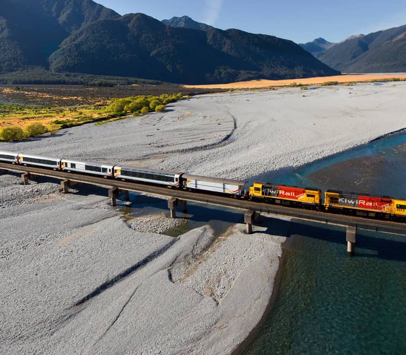 Train crossing bridge over river with mountains in background on a sunny day Credit: Pure Discoveries
