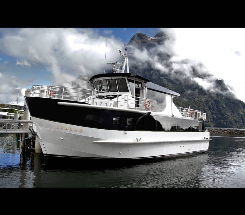 Sinbad ferry boat docked at Milford Sound with mountains and clouds in the background. Credit: Real Journeys