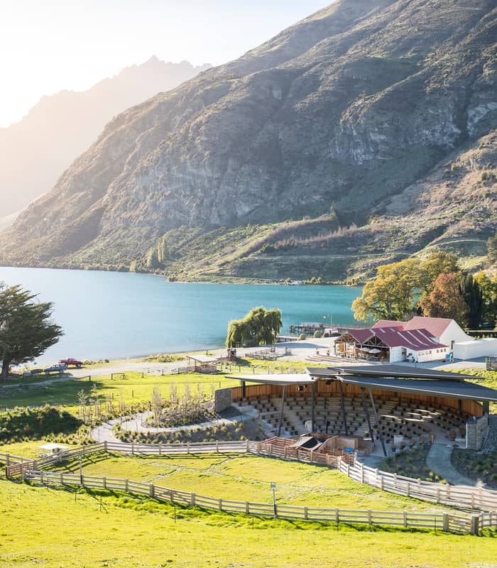 Amphitheatre and farm buildings beside a lake with mountains in the background under sunlight. Credit: Real Journeys