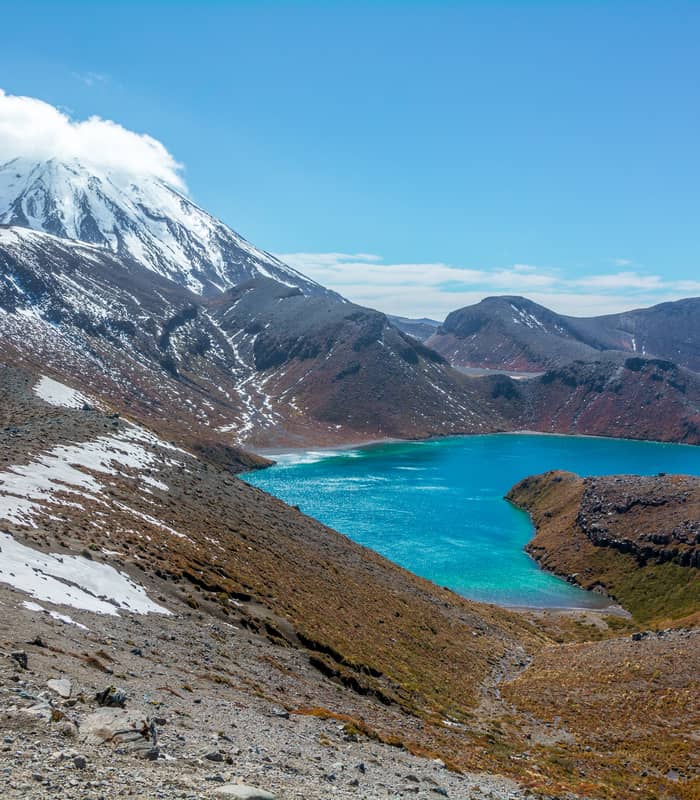 Snow-capped Mt Ngauruhoe with a bright blue lake in the volcanic landscape under a clear sky.