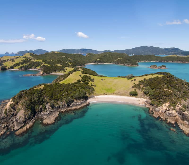 Aerial view of green island with beaches and turquoise water under blue sky. Credit: Cheeky Kiwi Travel