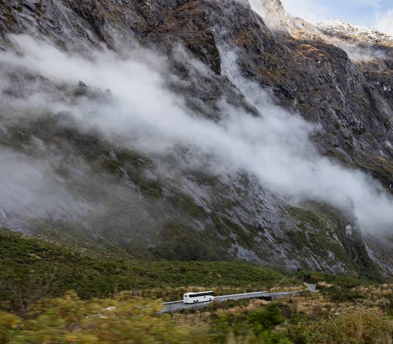 Bus driving on mountain road with fog and cliffs in background. Credit: Entrada - Gray Line / Great Sights
