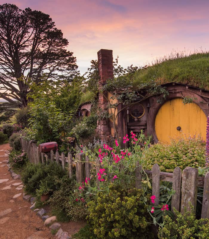 Hobbit hole with a yellow door and garden at sunset on the Hobbiton movie set. Credit: Cheeky Kiwi Travel