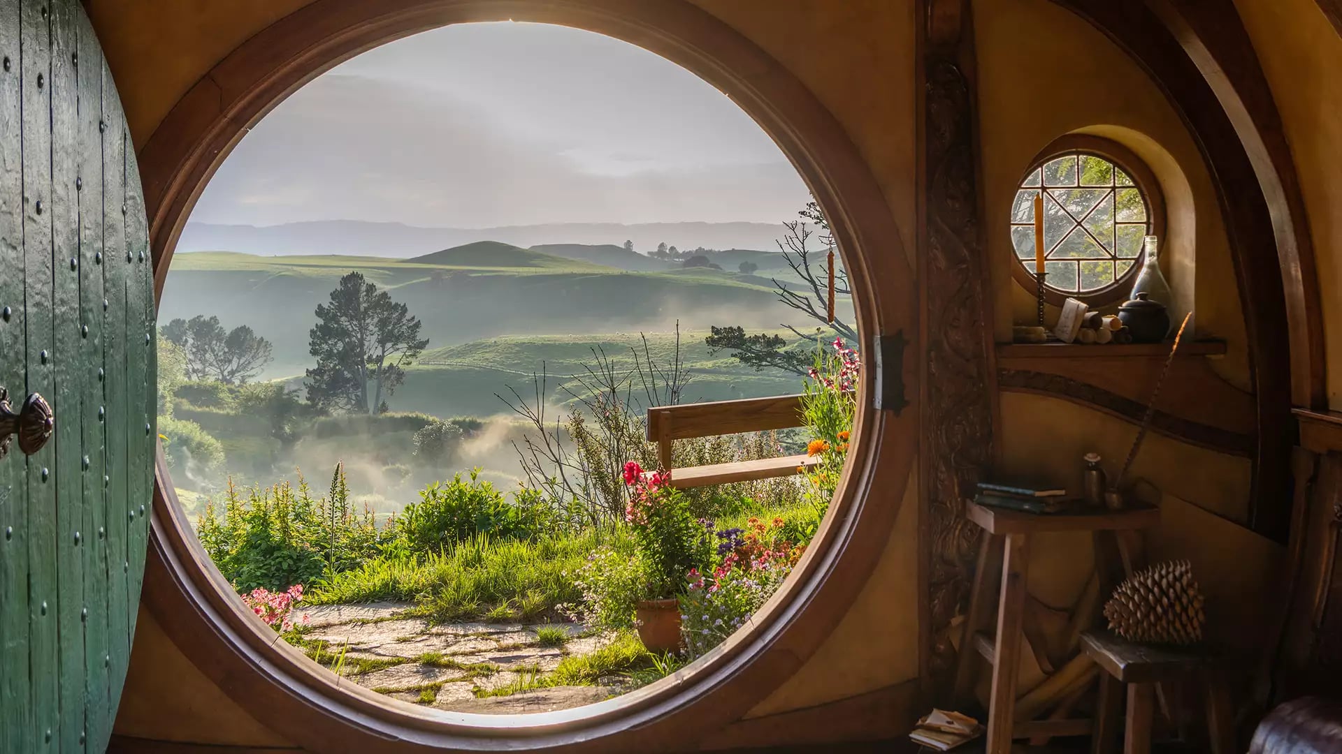 Inside view of a hobbit hole with a round door open to a green garden and rolling hills beyond. Credit: Hobbiton Movie Set Tours