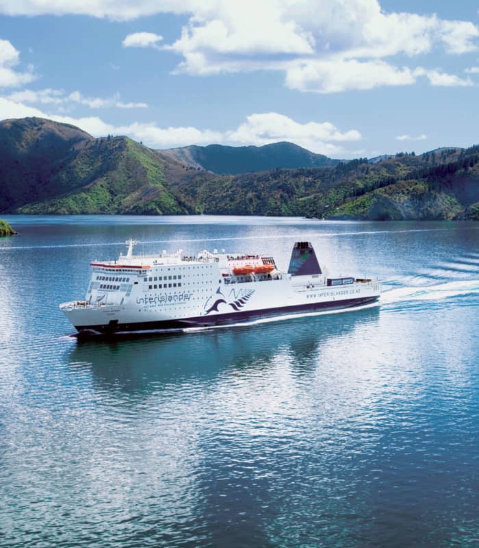 Interislander ferry sailing on blue water with green hills and clouded sky Credit: Intrepid Travel