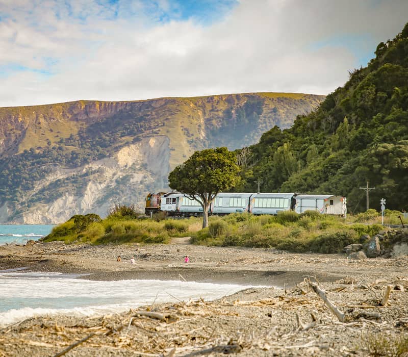 Train moving along beach coastline with mountains and ocean in the background. Credit: Kiwi Rail
