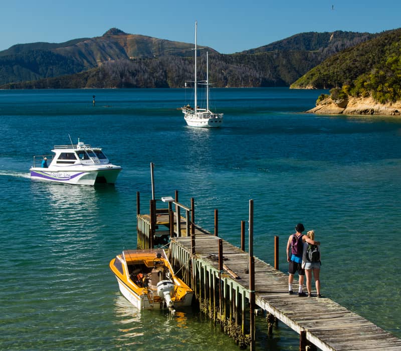 Small boat approaching dock with couple, mountains and clear water in background. Credit: Marlborough Tour Company