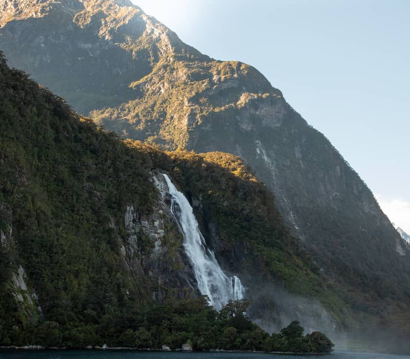 Waterfall flowing down a mountain into a river with forest and clear sky. Credit: Altitude Tours