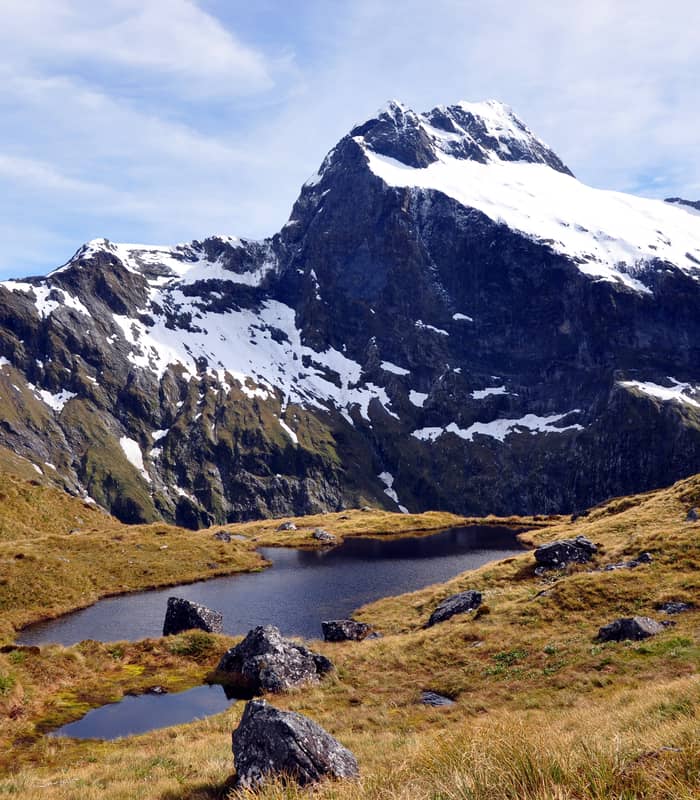 Snow-capped mountain behind a small alpine lake with grassy and rocky terrain. Credit: Fine Tours Group
