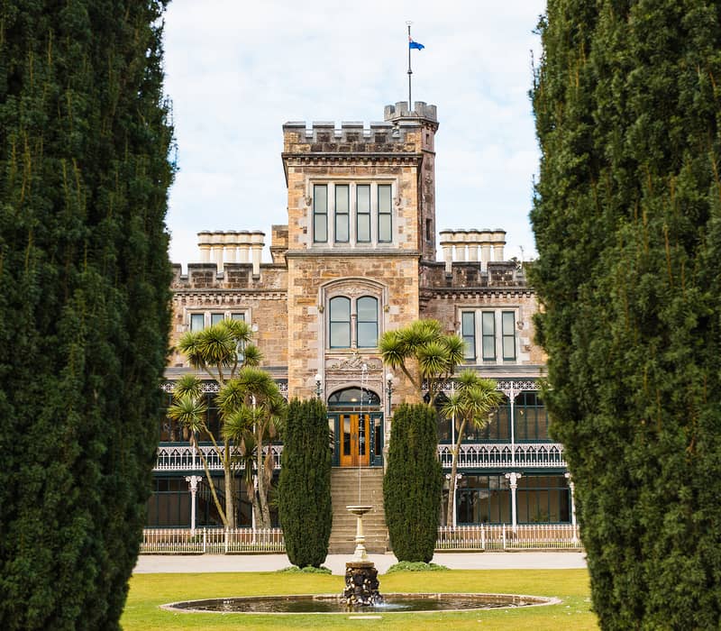 Larnach Castle viewed through tall hedges with a fountain and garden in front. Credit: Monarch Wildlife