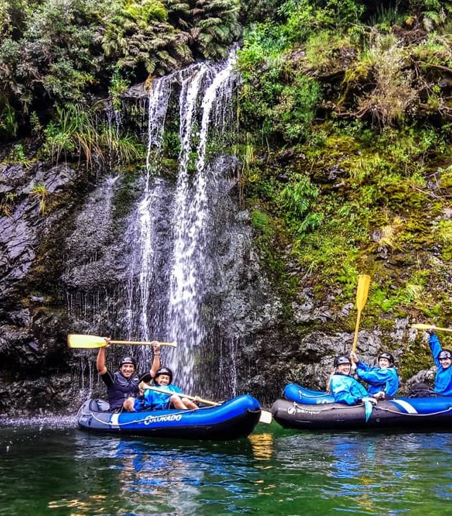 People kayaking in blue rafts near a waterfall with green forest and rocks. Credit: Pelorus Eco Adventures