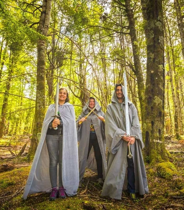 Three people wearing capes and holding swords pose in a bright green forest. Credit: Pure Glenorchy