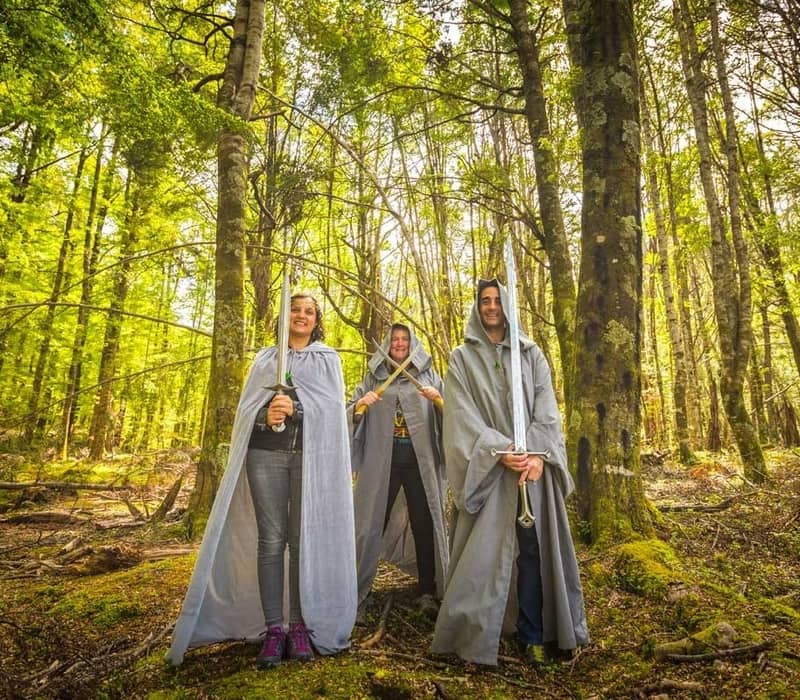 Three people wearing capes and holding swords pose in a bright green forest. Credit: Pure Glenorchy
