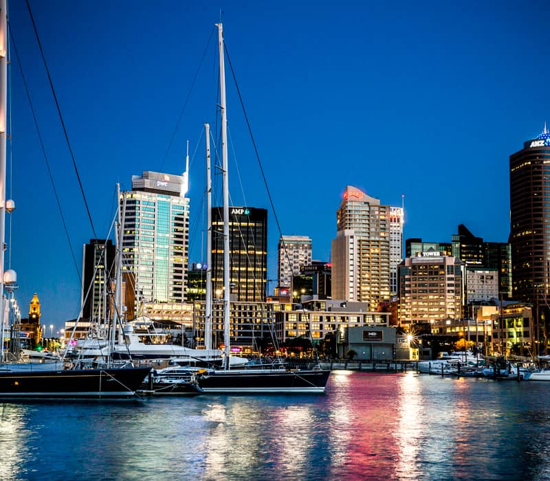 Auckland waterfront at night with boats docked and city lights reflecting on water. Credit: Pure Discoveries