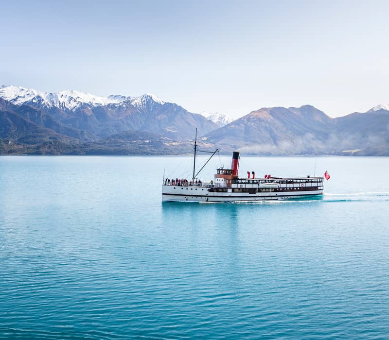 Steamboat cruising on blue lake water with snowy mountains in the background on a clear day. Credit: Real Journeys