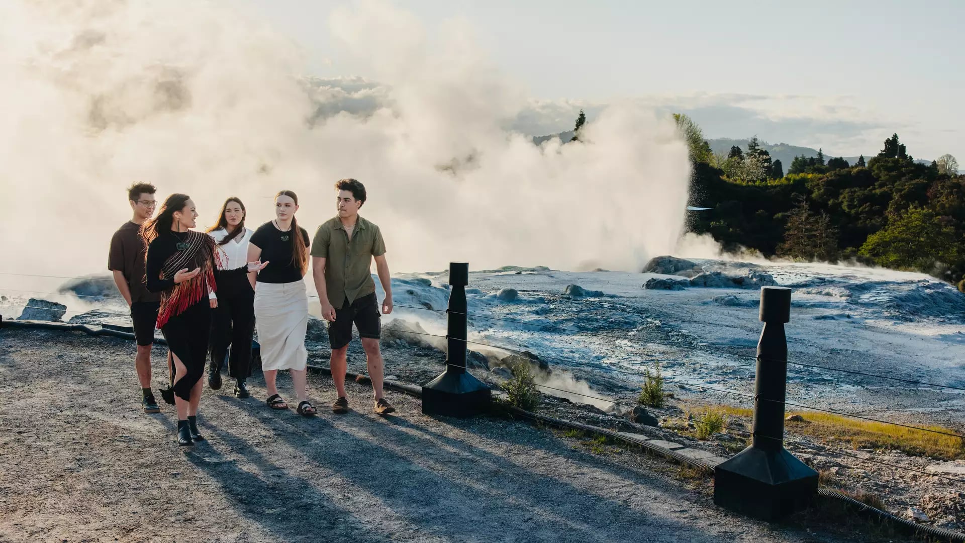 Group of people walking near a steaming geyser in a natural outdoor setting. Credit: Te Puia