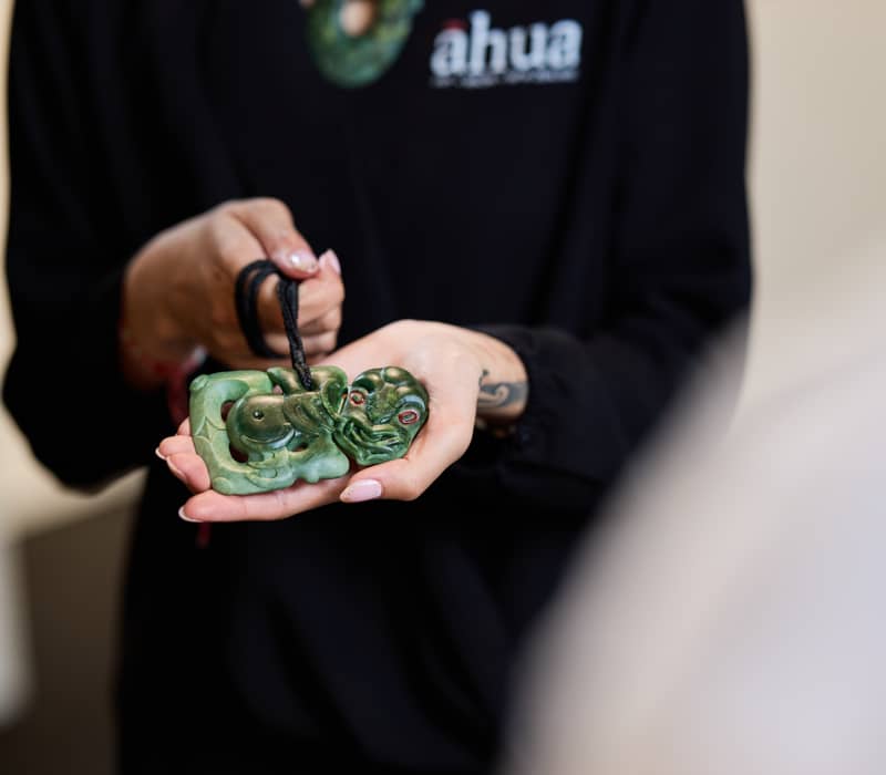 Hands hold a carved green jade pendant on a black rope. Credit: Te Puia