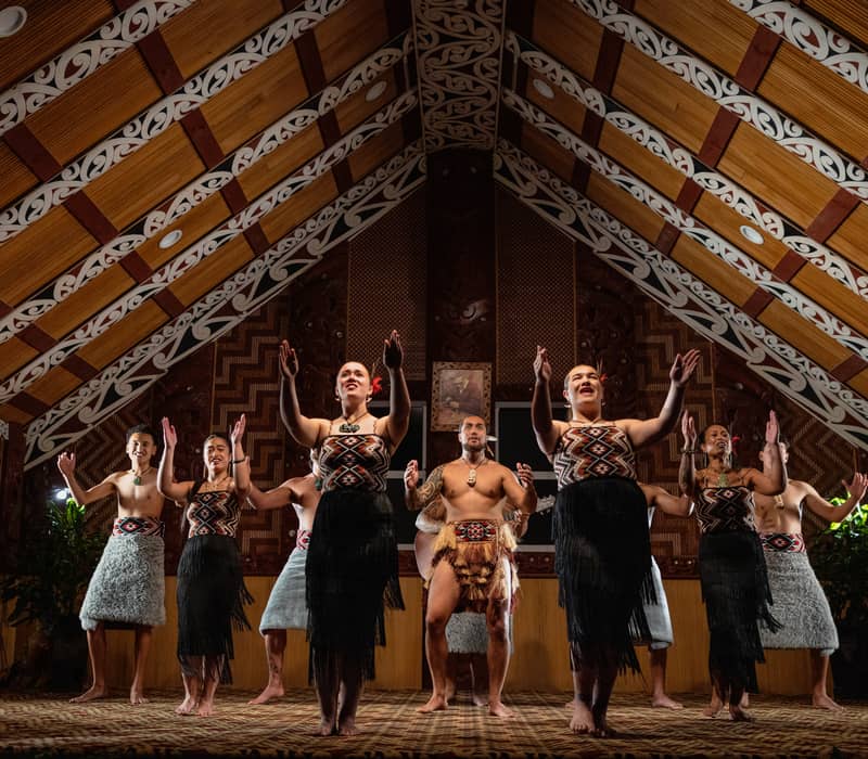 Performers in traditional Maori dress doing a group dance inside a decorated meeting house. Credit: Te Puia