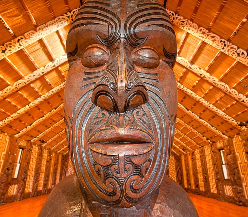 Close-up of a detailed Maori wood carving with tribal patterns inside an ornately decorated traditional building. Credit: Waitangi Treaty Grounds
